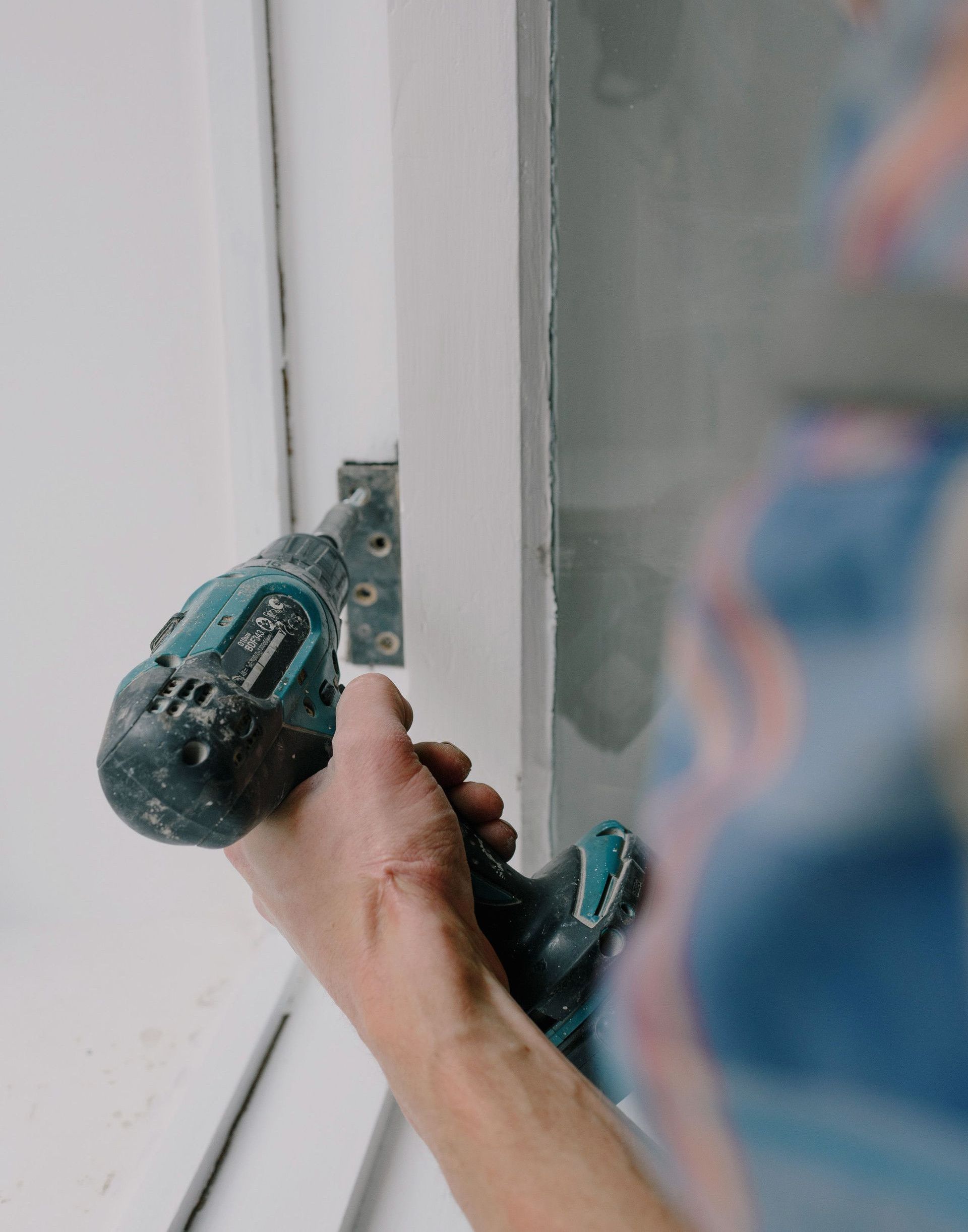 Crop bearded guy installing new wooden window with contemporary screwdriver and metal hinge during renovation process in apartment